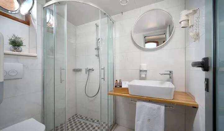 Compact bright cabin bathroom with glass shower and round mirror
