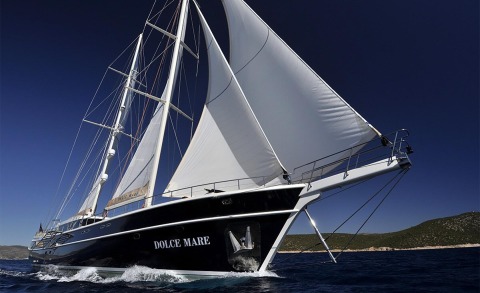 Dolce Mare sailing yacht with white sails on deep blue sea and coastline in background