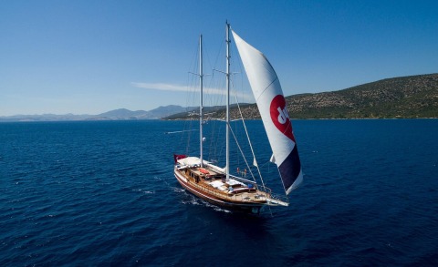 Grace 1 sailing yacht with large white sails on blue sea near coastline