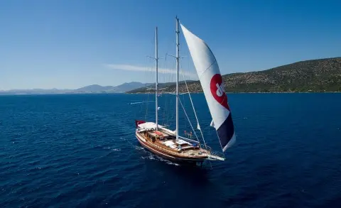Grace 1 yacht with white sails on blue sea, rocky coastline in distance