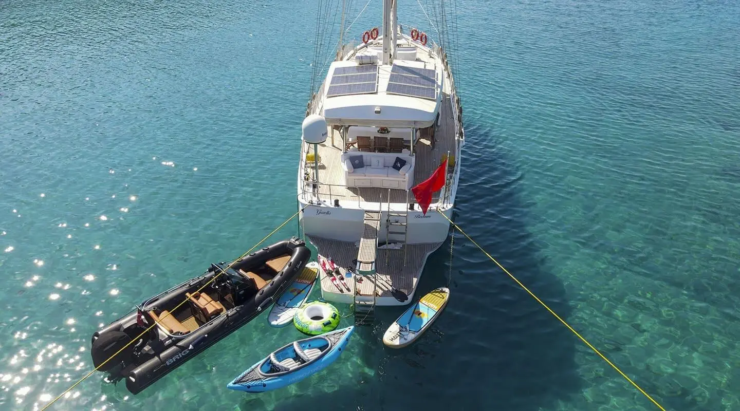 Gazella yacht anchored near a small inflatable boat and paddleboard in blue water