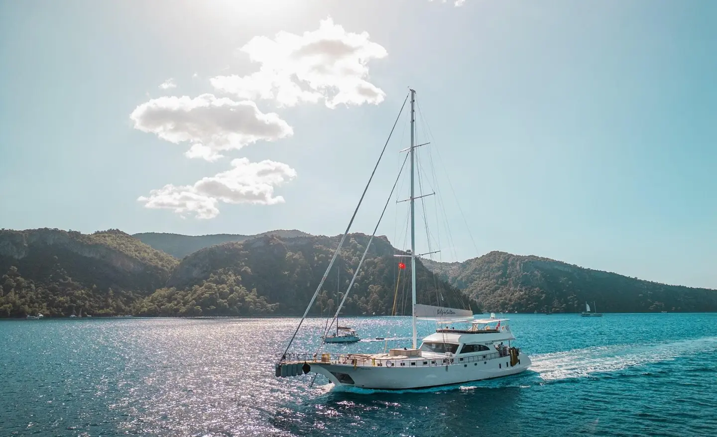 Belgin Sultan luxury gulet anchored at sunset with sails down near rocky coastline