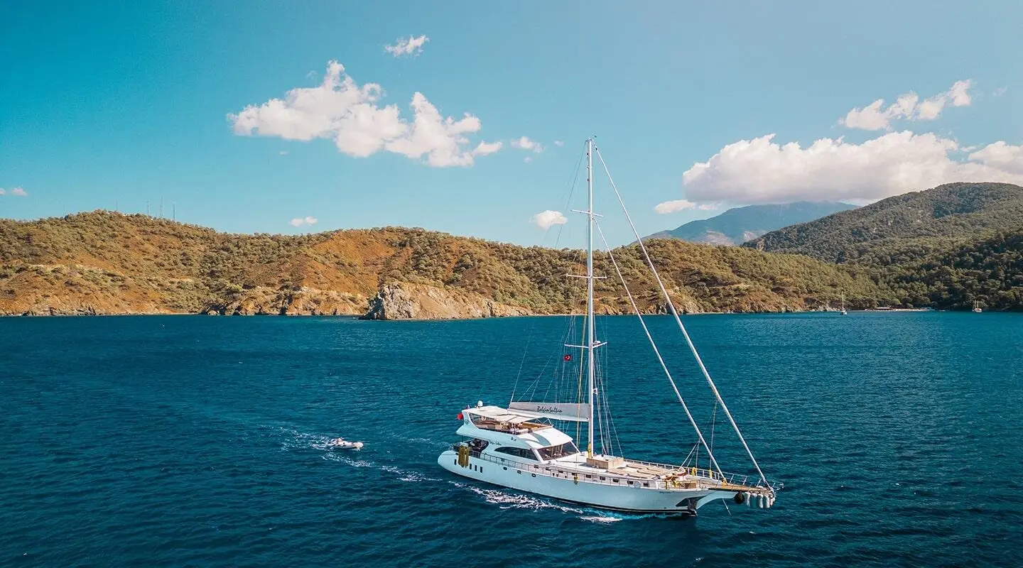 Belgin Sultan gulet sailing near rocky coastline under blue sky