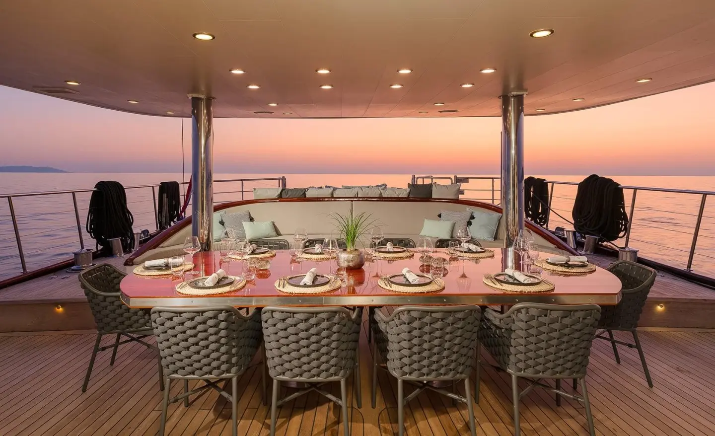 Large dining table with wicker chairs on an open deck at sunset