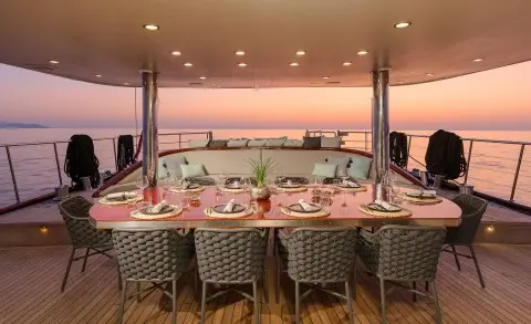 Large dining table with wicker chairs on an open deck at sunset