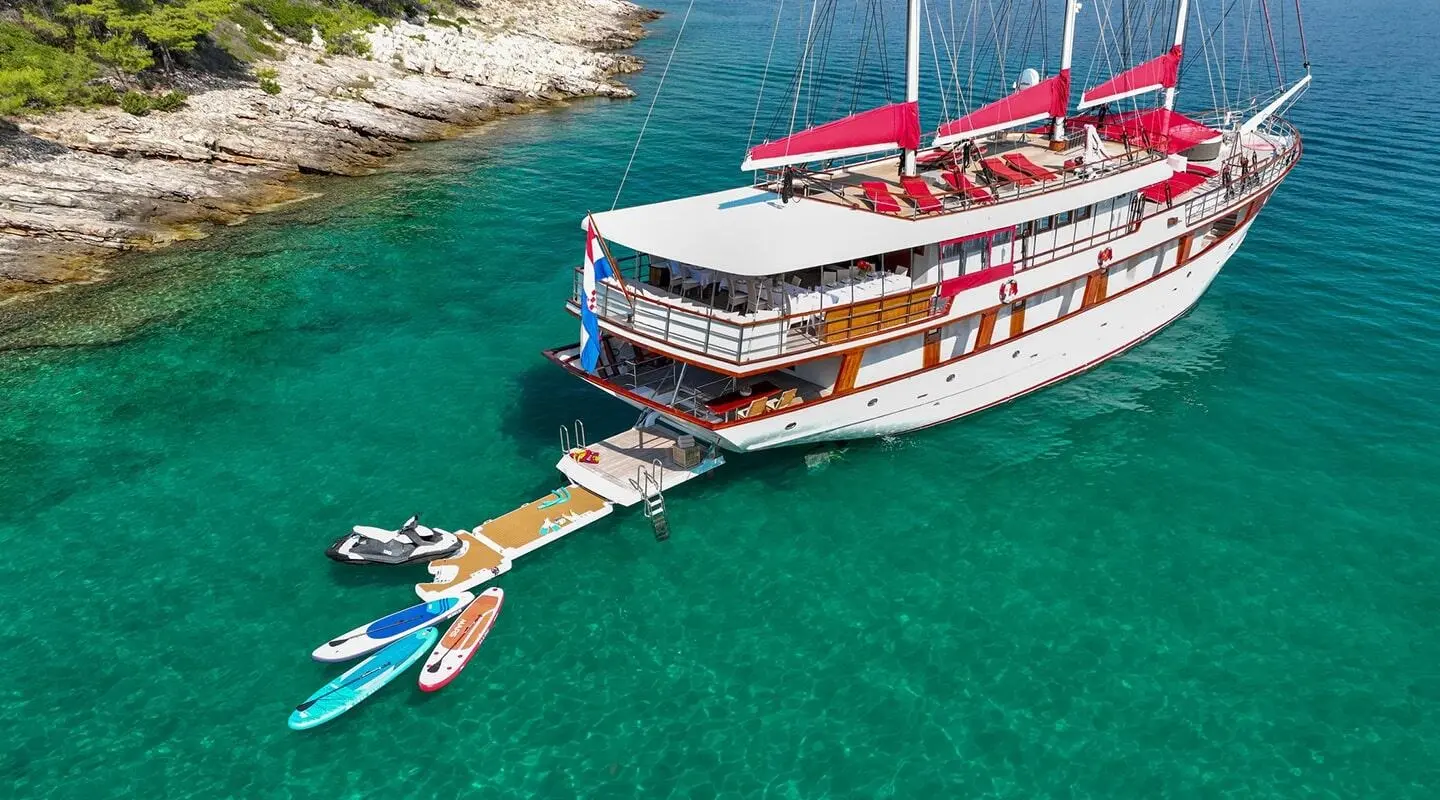 Yacht Barbara anchored in turquoise water with guests on deck and a small jet ski nearby