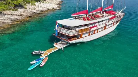Yacht Barbara anchored in turquoise water with guests on deck and a small jet ski nearby