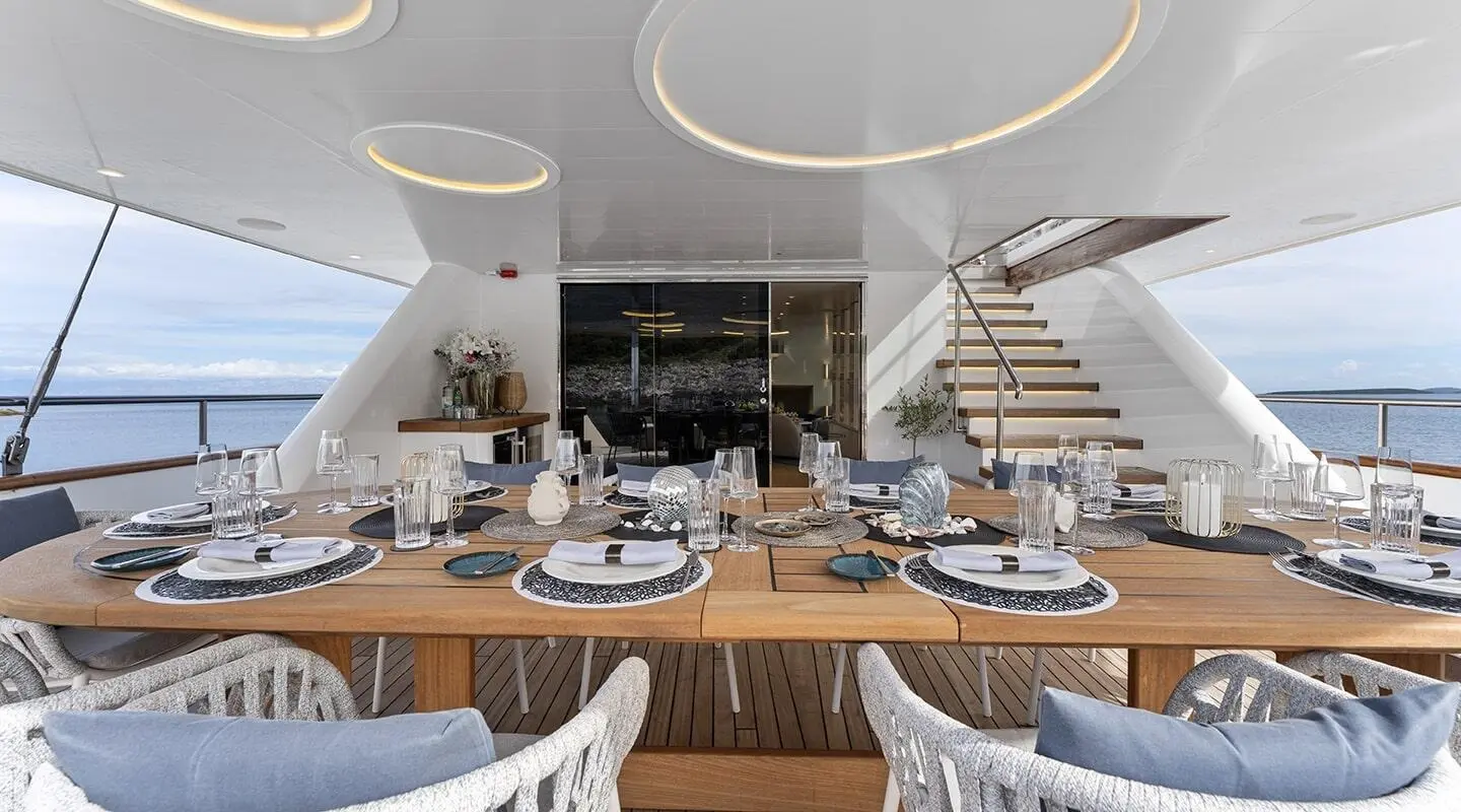 Maxita yacht dining on deck with long wooden table set for alfresco meal
