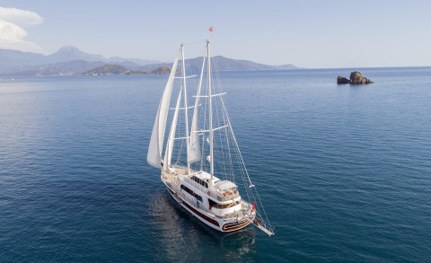 A sailing yacht on calm sea with distant rocky islets and mountains