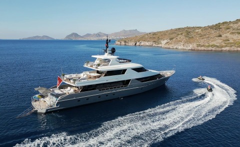 Large white luxury yacht Illusion II anchored near the shore with clear blue sea and hillside coastline in the background