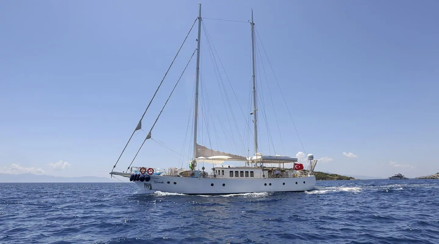 Gazella yacht at sea with sails lowered, white hull, blue sky and calm water
