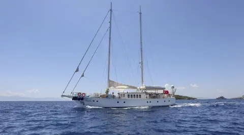 Gazella yacht at sea with sails lowered, white hull, blue sky and calm water