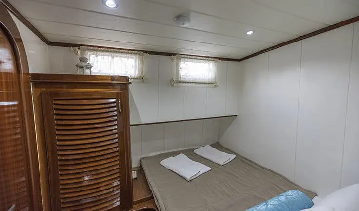Small bright cabin interior with two single beds and windowed portholes
