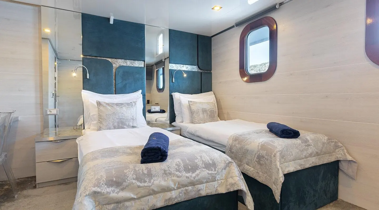 Two beds aboard the Yolo luxury yacht with beige bedding and blue accents