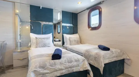 Two beds aboard the Yolo luxury yacht with beige bedding and blue accents