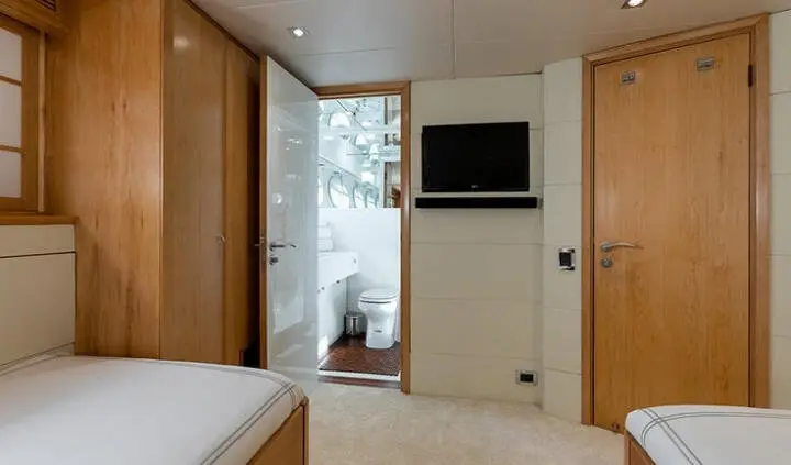 A cabin aboard a yacht with a bed, wardrobe, and a small TV mounted on the wall.