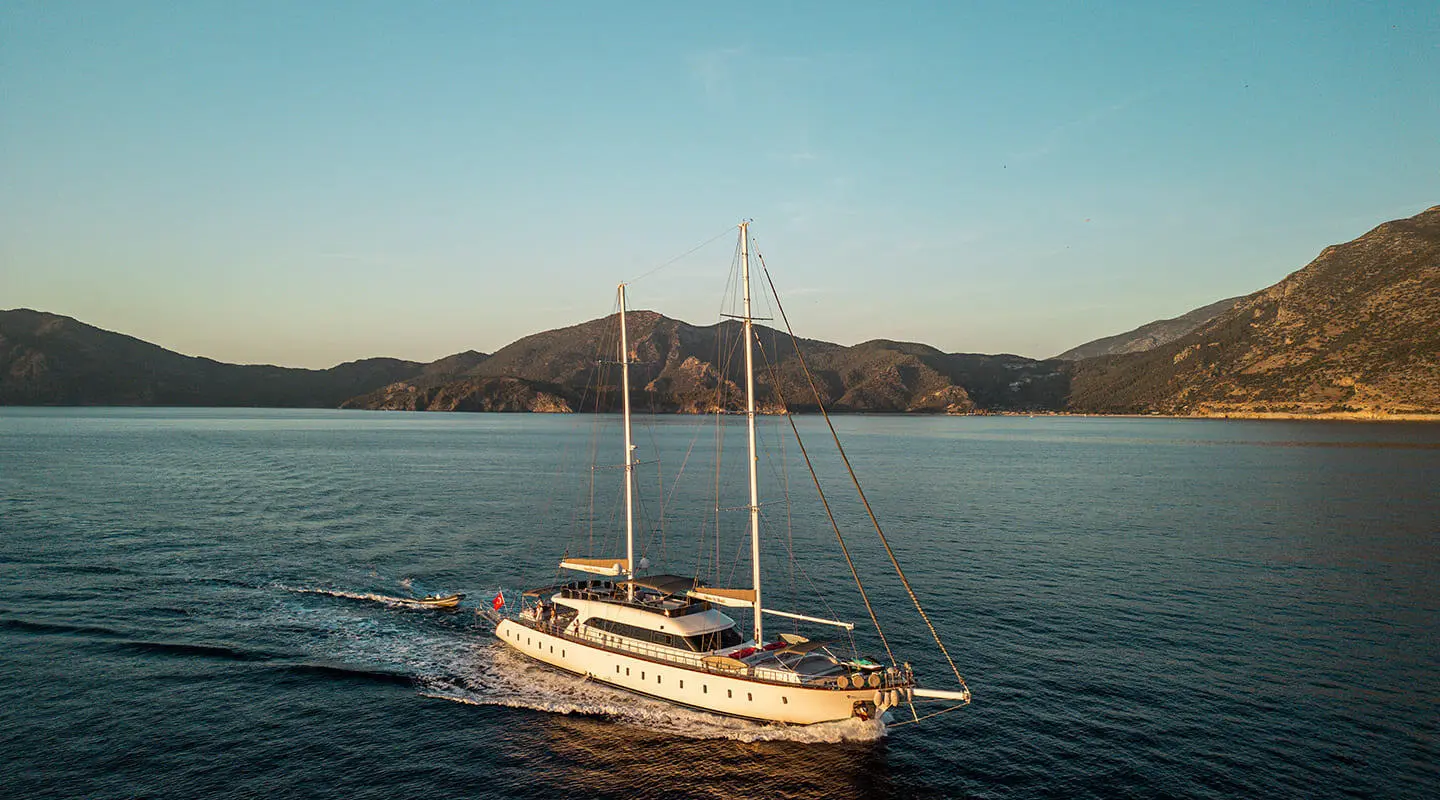 Queen Of Makri yacht anchored in calm blue water at sunset with hills in background