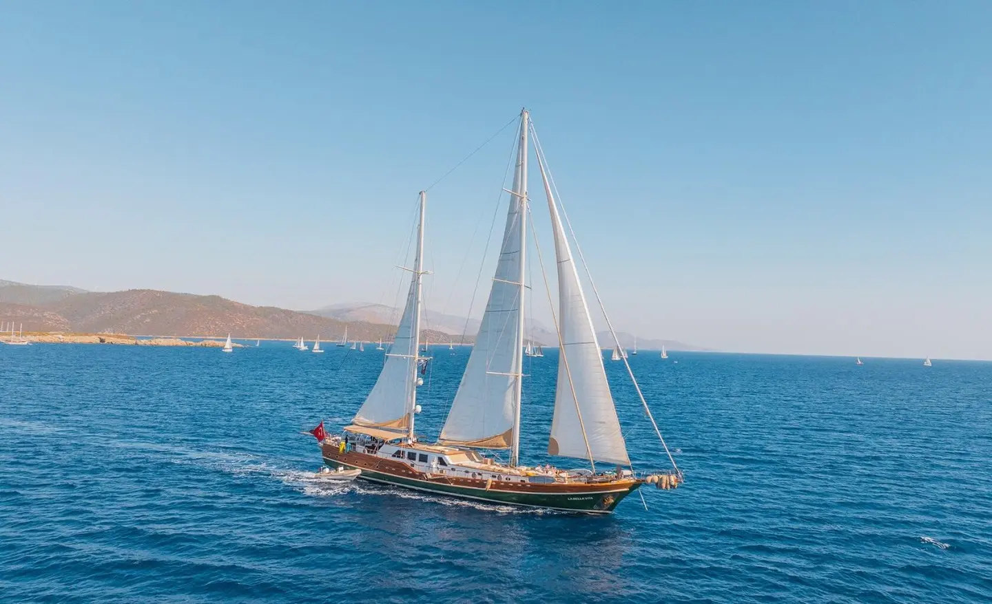 La Bella Vita sailing yacht on blue sea with sails full, coastal shore in background