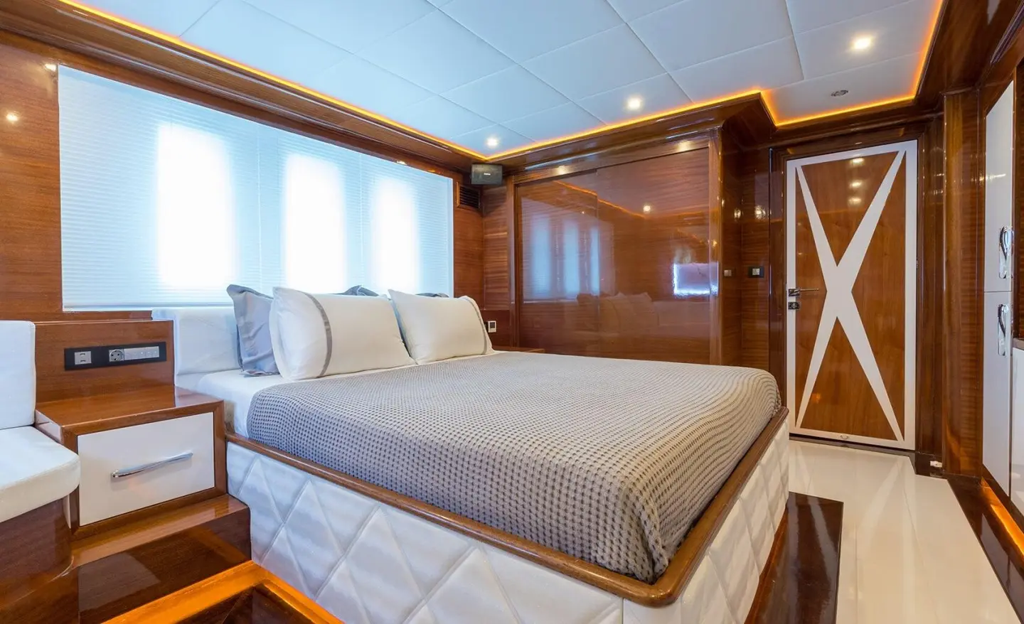 Cozy yacht bedroom with bed, pillows, wood panels, and windows showing outside light