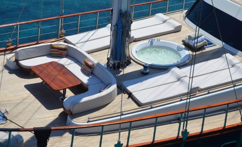 Blue Heaven yacht deck with white seating, wooden table, spa tub and calm blue sea backdrop