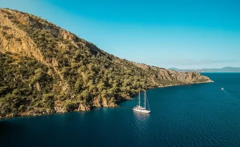 Yacht Angelo III anchored along a rocky coast at sunset with calm blue water