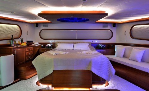 Interior of a yacht bedroom with a large bed, wooden cabinets and side consoles, soft lighting