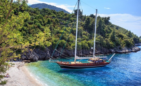 Carpe Diem 7 sailing yacht anchored near a rocky lush coastline with clear turquoise water