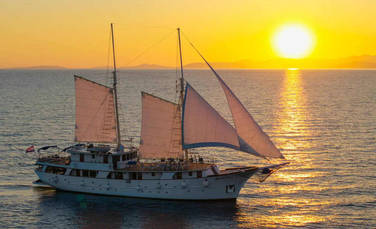 Mendula sailing yacht under sunset with white hull and sails in golden light