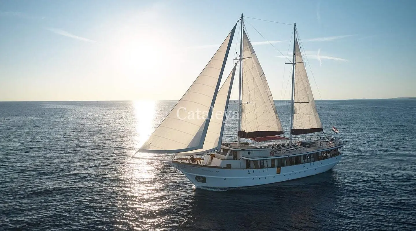 Cataleya gulet sailing yacht with white sails on calm sea at sunset
