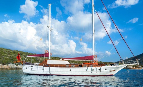 Primadonna gulet anchored with white hull and wooden deck yacht, tall masts, calm blue sea and clear sky