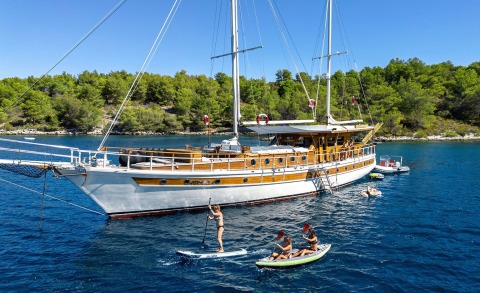 Gulet Aborda yacht anchored near shore with people on deck and water sports gear nearby