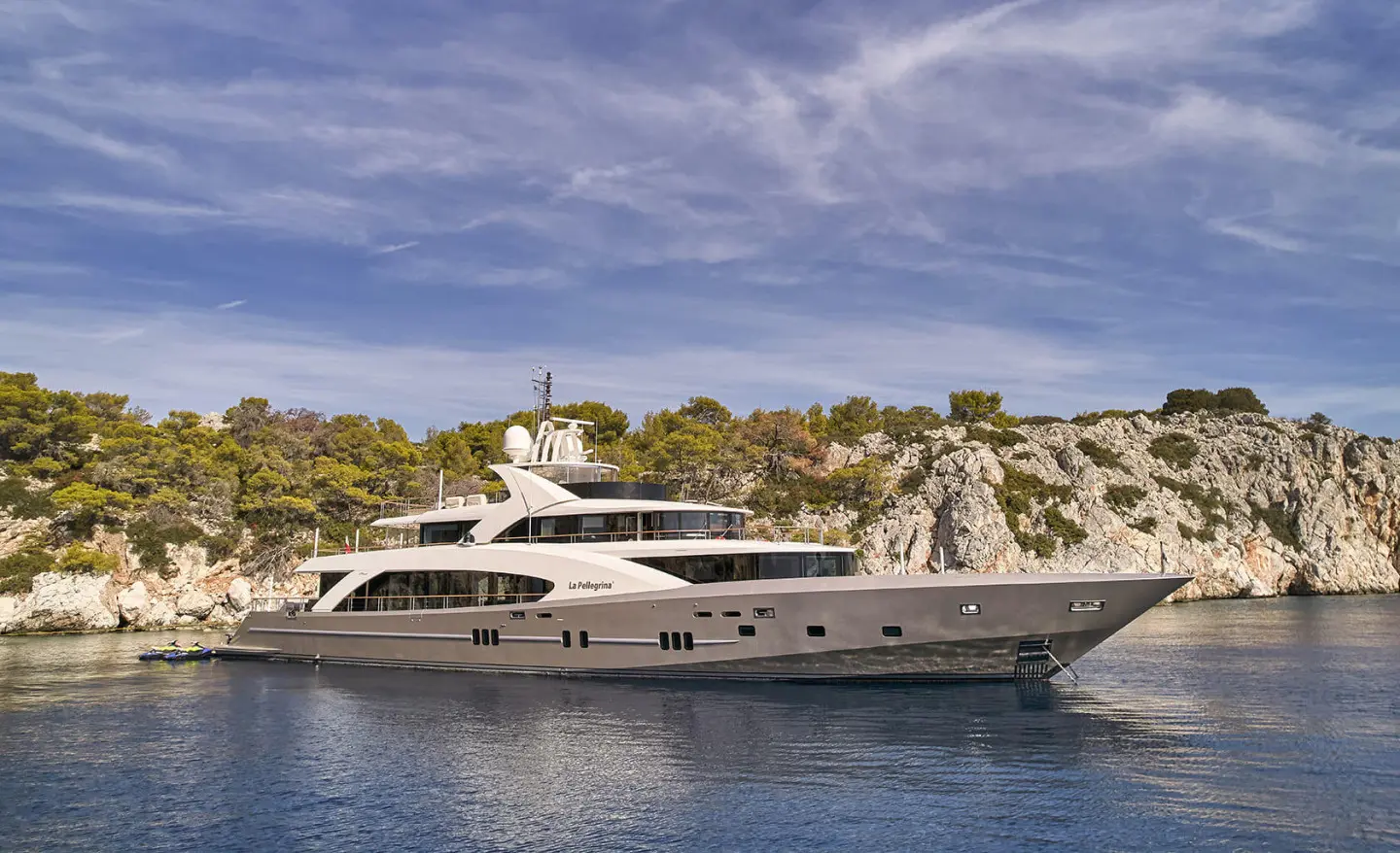 Grey motor yacht anchored beside rocky coastline with blue sky