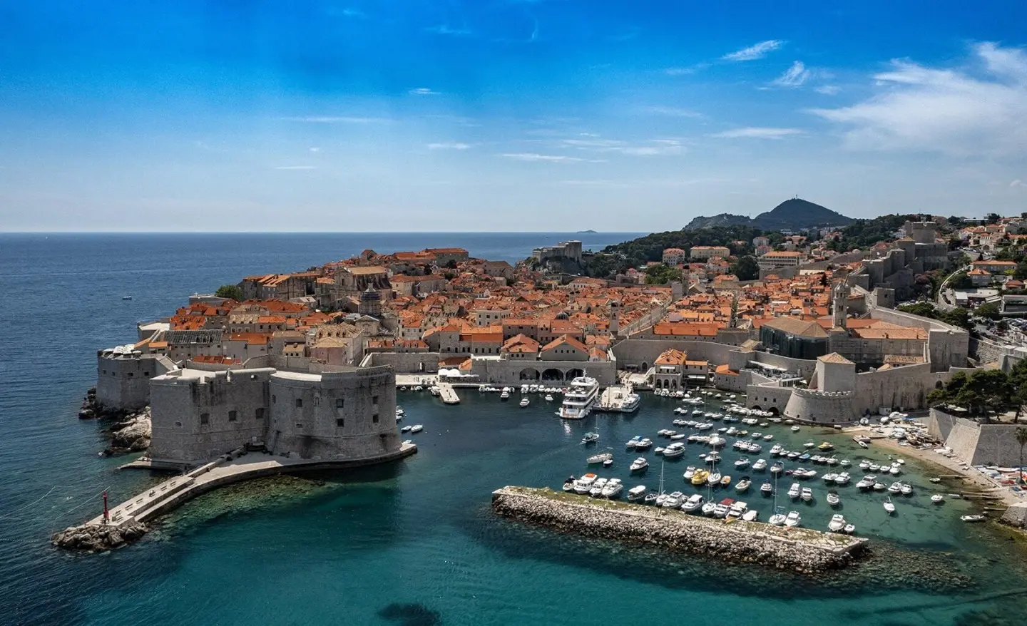 Yolo yacht docked in Dubrovnik harbor with boats and red-tiled buildings