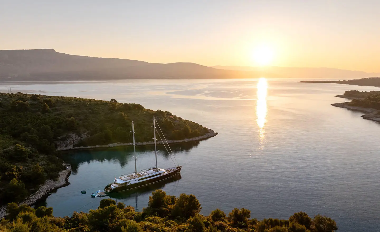 Nocturno yacht at sunset overlooking calm sea and rocky coastline