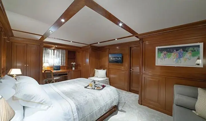 Aquila cabin shows a bed with white linens, wooden walls, built-in cabinetry, and ceiling beams.