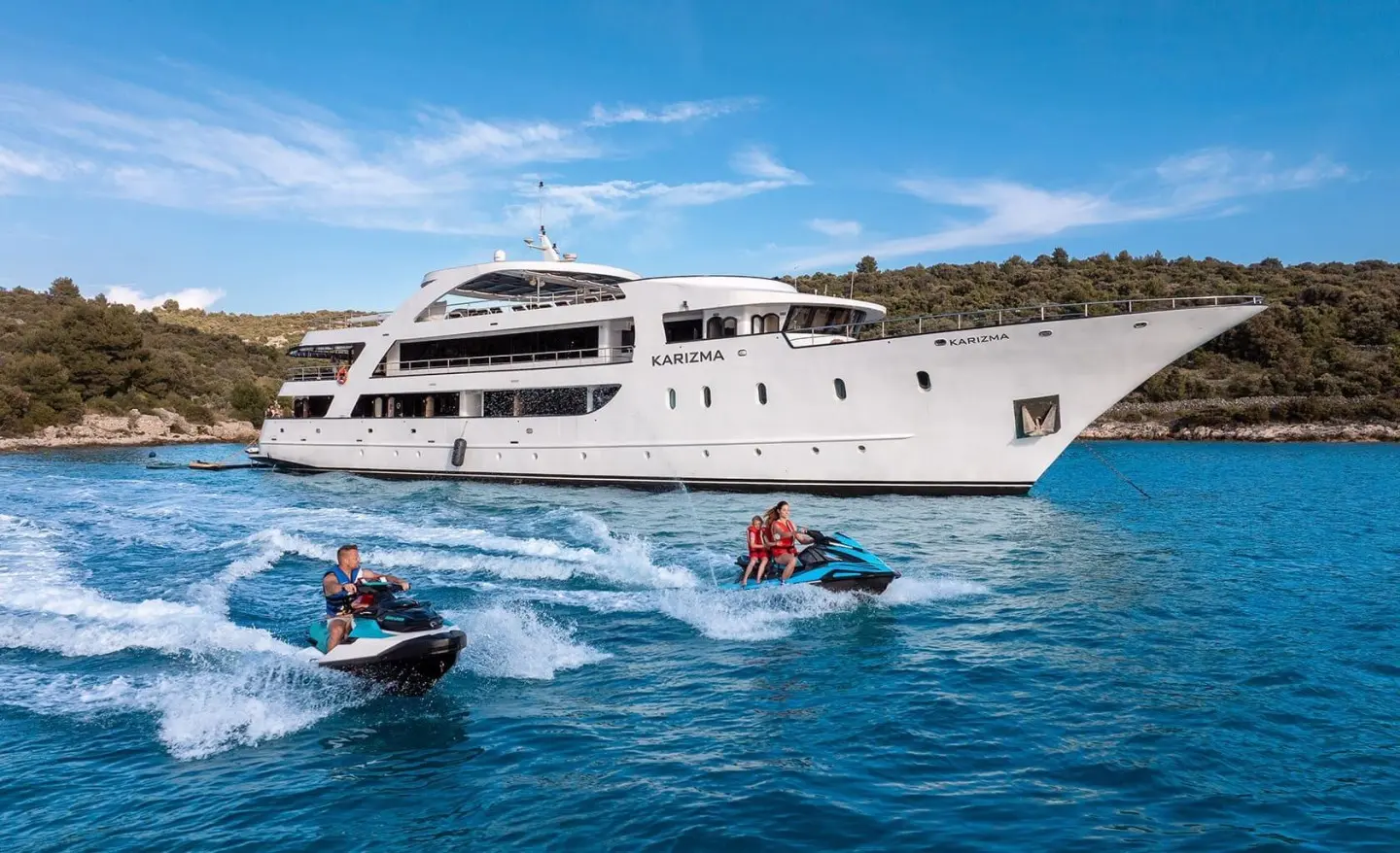 Karizma yacht exterior anchored in blue water with people jet skiing nearby