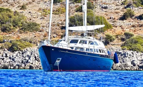 Blue motor yacht Tamarita anchored near rocky shore, clear water around