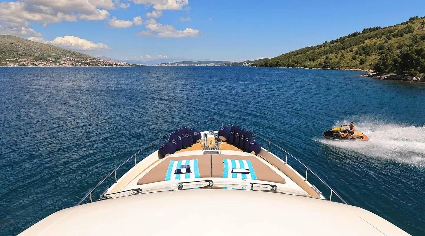 A yacht bow deck view with sun loungers facing blue sea and distant shoreline