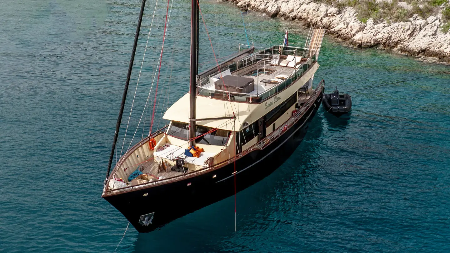 Yacht Santa Clara anchored in clear blue water, top deck visible
