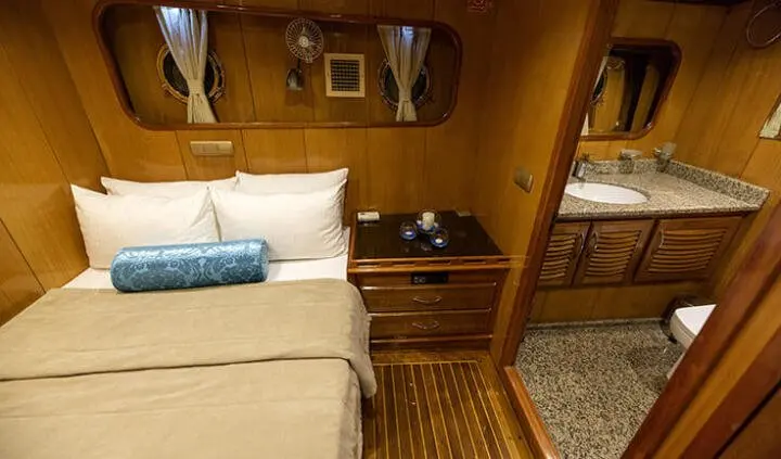 Master cabin with king bed, beige linens, wooden nightstands and mirrored wardrobe