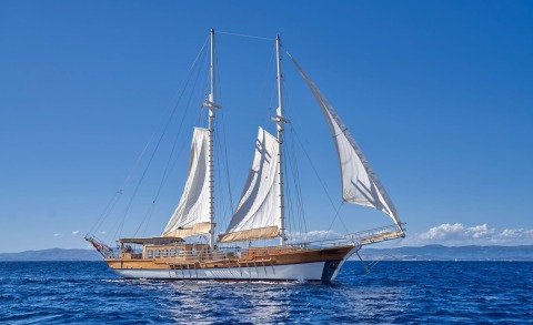 Two-masted wooden sailing yacht with white sails gliding on blue open sea under clear sky