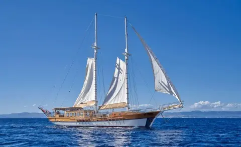 Libra yacht with white sails on calm blue sea at sunset, classic sailing ship