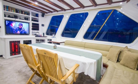 Indoor yacht salon with a TV, shelves, wooden chairs, and a seating area
