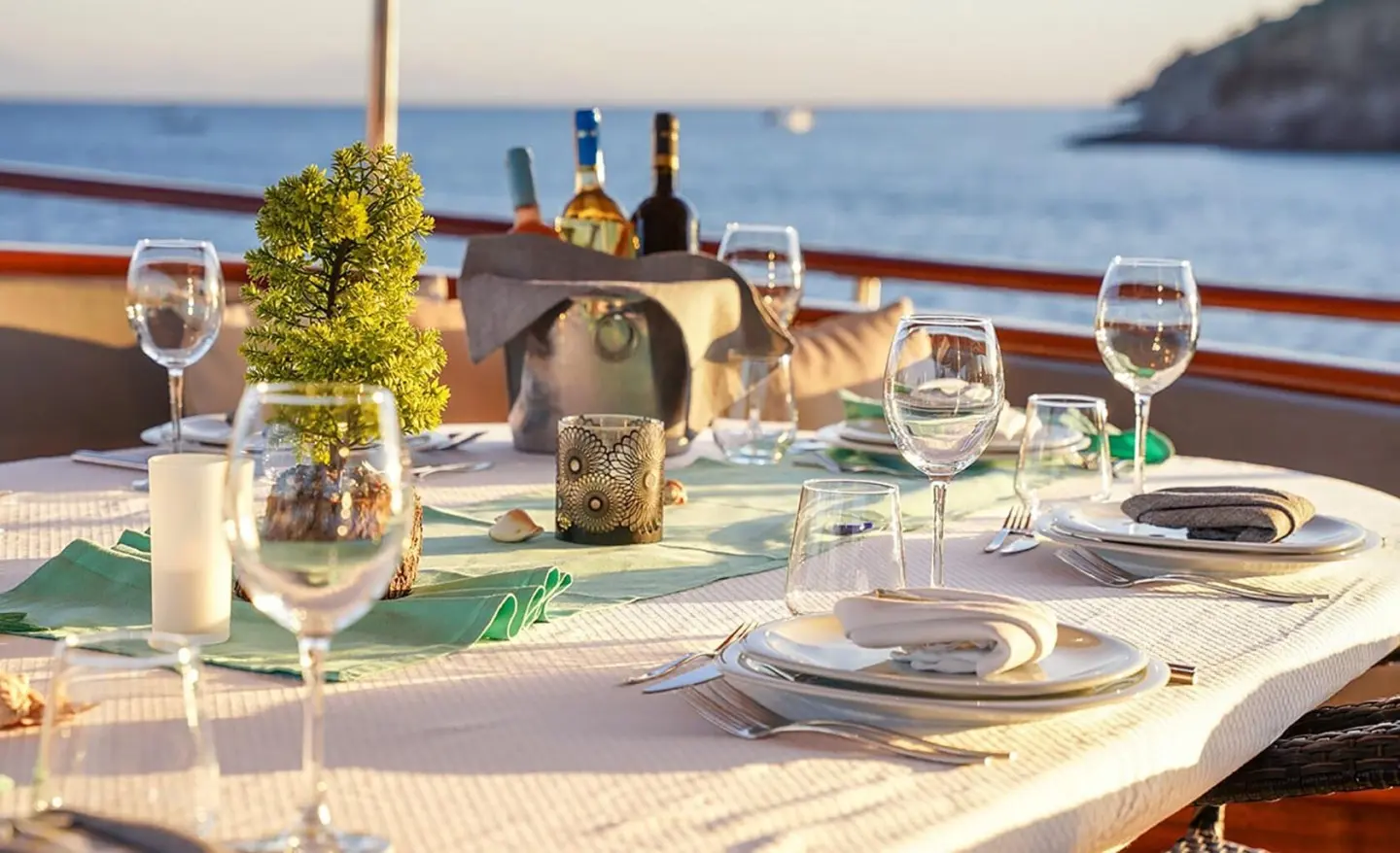Table on yacht with decorative plant and bottles, sea view at sunset