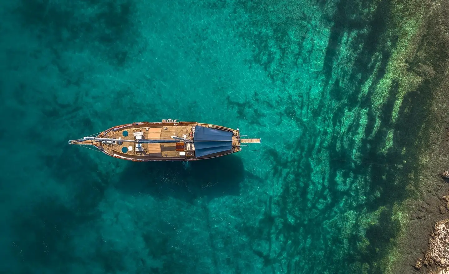 Small wooden yacht named Smart Spirit anchored in crystal clear turquoise water at sunset