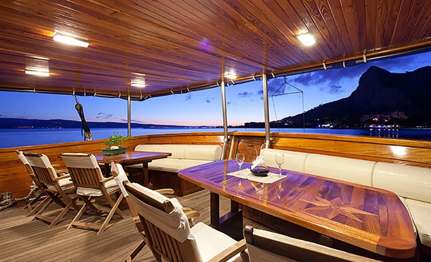 Tajna Mora luxury Gulet at sunset with wooden deck seating and string lights