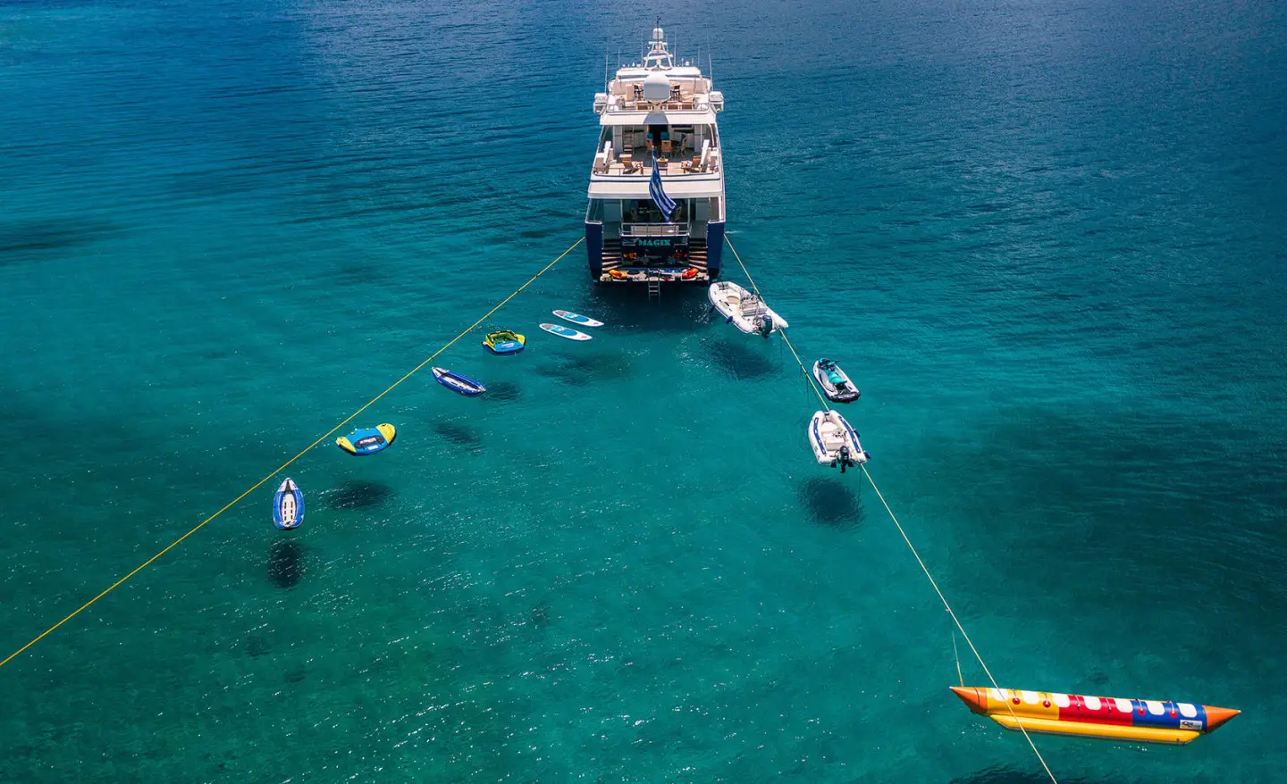 Luxurious motor yacht Magix anchored in clear turquoise water with a small boat nearby