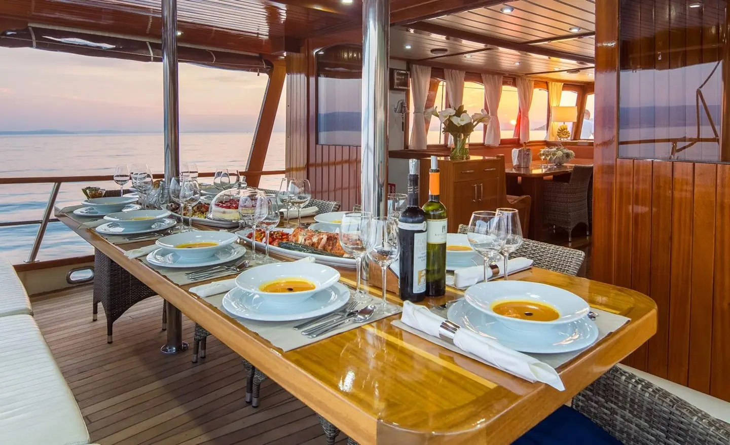 Yacht Altair dining on a sunset-lit deck with plates, wine bottles and chairs