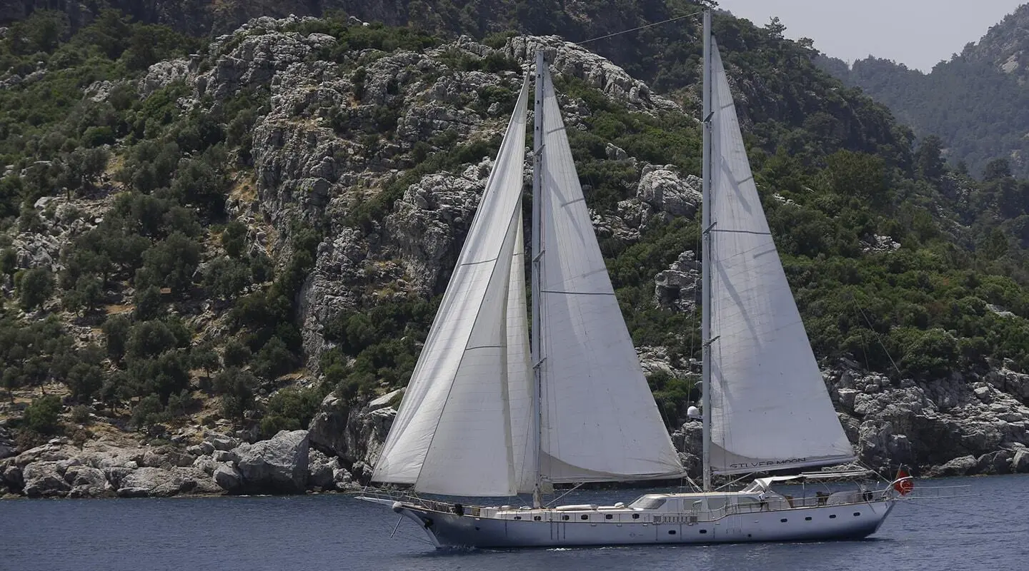 Sailing gulet Silver Moon with white sails on blue sea near rocky coastline