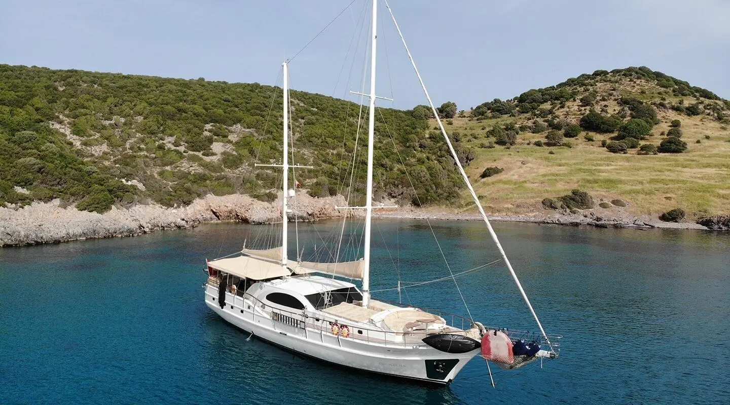 White sailing gulet anchored in a calm cove with two masts and deck lounge